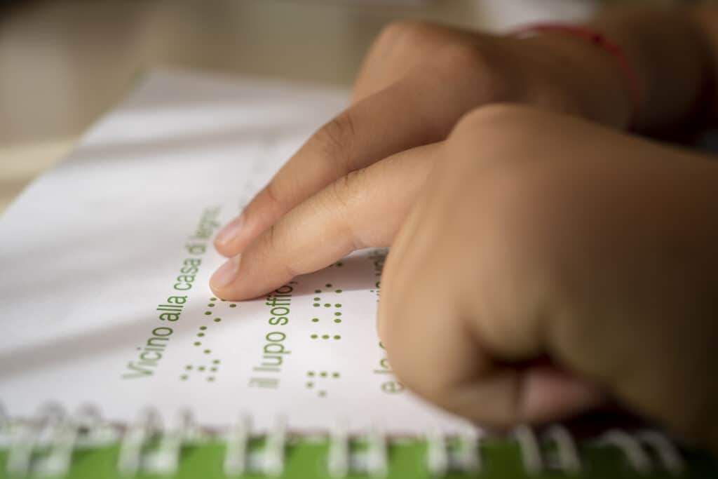 Le dita di un bambino leggono il Braille e i caratteri in nero.