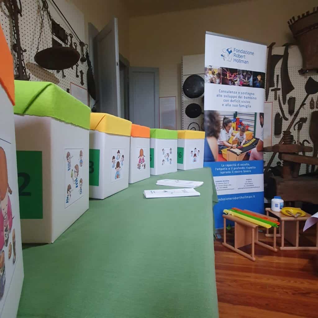 interno del museo etnografico di villa Giulia a Cannero: allestimento del laboratorio multisensoriale della Fondazione con alcune scatole da esplorare con le mani. Sul fronte delle scatole c'è una facilitazione per bambini con deficit visivo. Sullo sfondo della stanza il roll up della fondazione Hollman