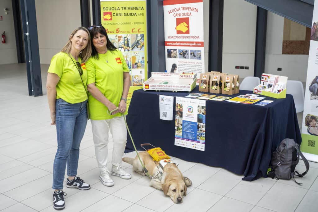 two volunteers and a dog from the Triveneta Guide Dog School in front of their illustrative banquet at the san gaetano cultural center