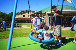 due genitori spingono due bambini seduti nell'altalena inclusiva a guscio del parco