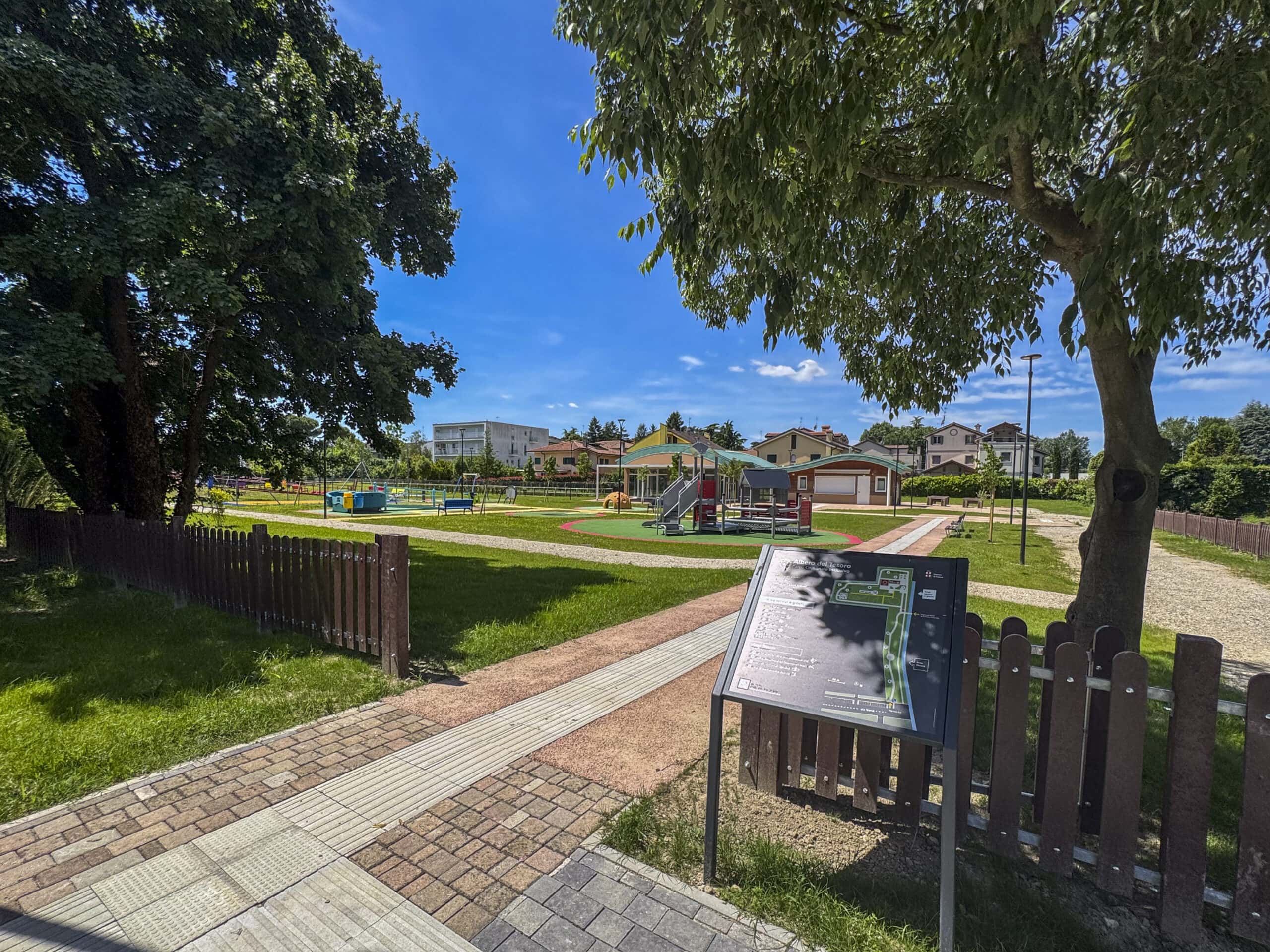 panoramica del parco inclusivo "Albero del tesoro". A destra la mappa tattile, al centro il camminamento con i logges e sullo sfondo l'area aggregativa, i giochi accessibili e il verde in cui è immerso il parco.