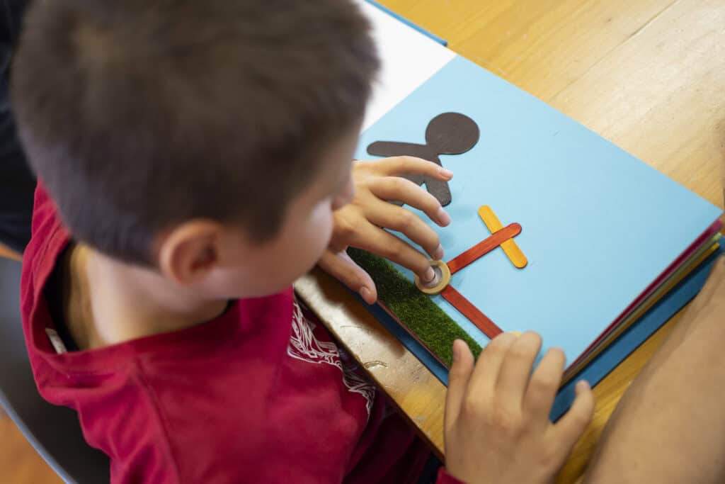 Un bambino di spalle tocca con le dite l'immagine tattile di un libro che rappresenta un monopattino.